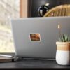 A sleek laptop with a printed photo sticker on the back, placed on a modern workspace with a plant and notebook.