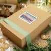 An elegant holiday gift box with a watercolor sailboat art print, surrounded by Christmas cookies and decorations.